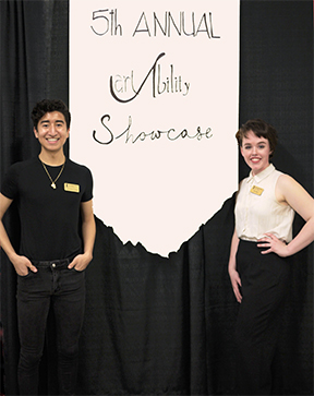 Two trainees, a man and a woman, standing on either side of a large banner for the 5th Annual Art Ability Showcase