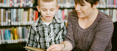 A teacher is showing a young boy a book, pointing to a word on the page.